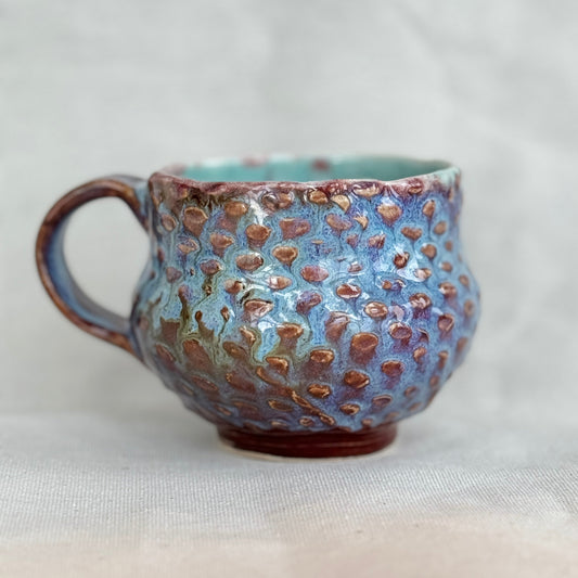 Ceramic mug with textured blue and brown surface on a light background