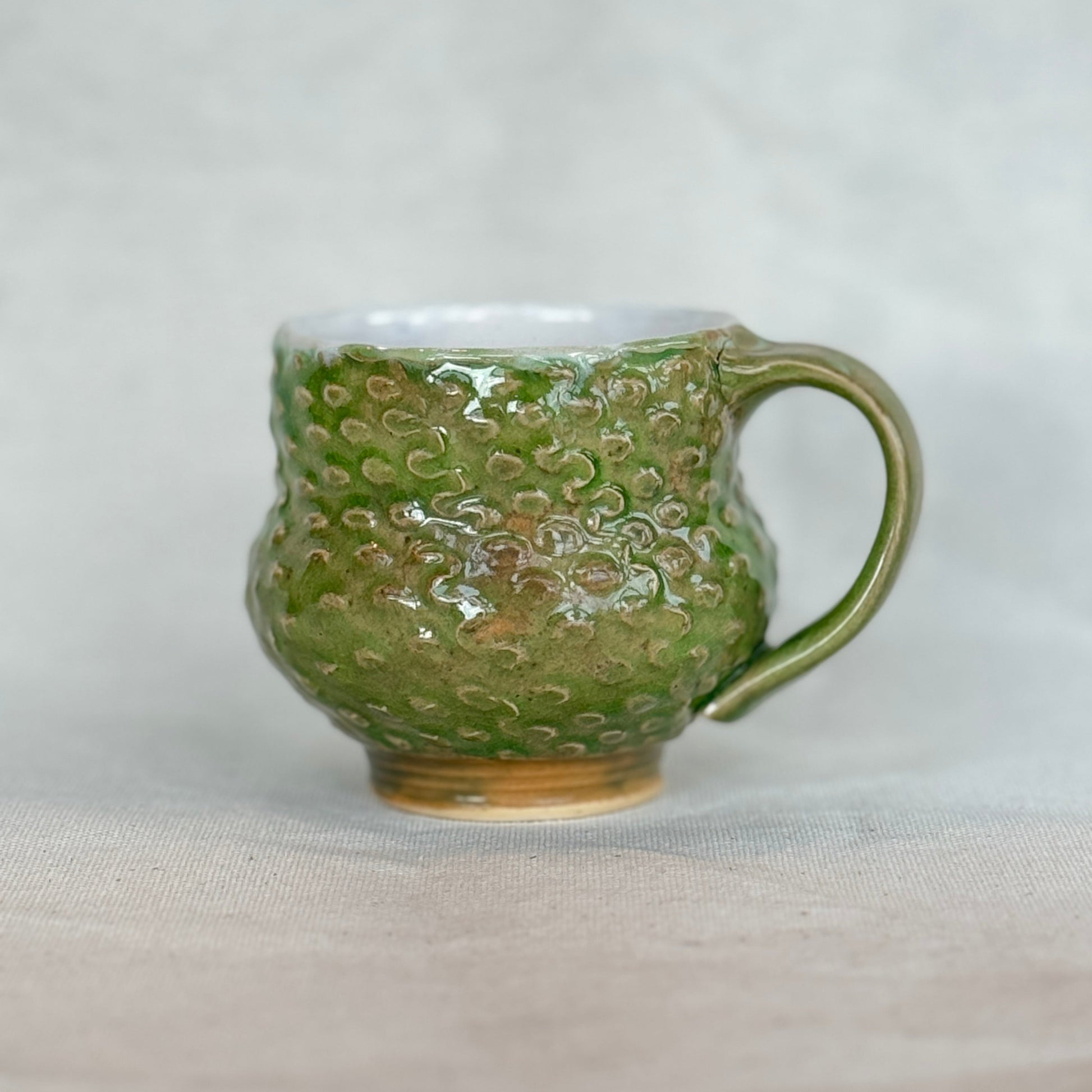 Green ceramic mug with textured surface on a light gray background