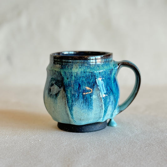 Blue ceramic mug with black rim and handle on a light gray background
