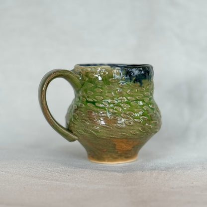 Green ceramic mug with textured surface on a light gray background