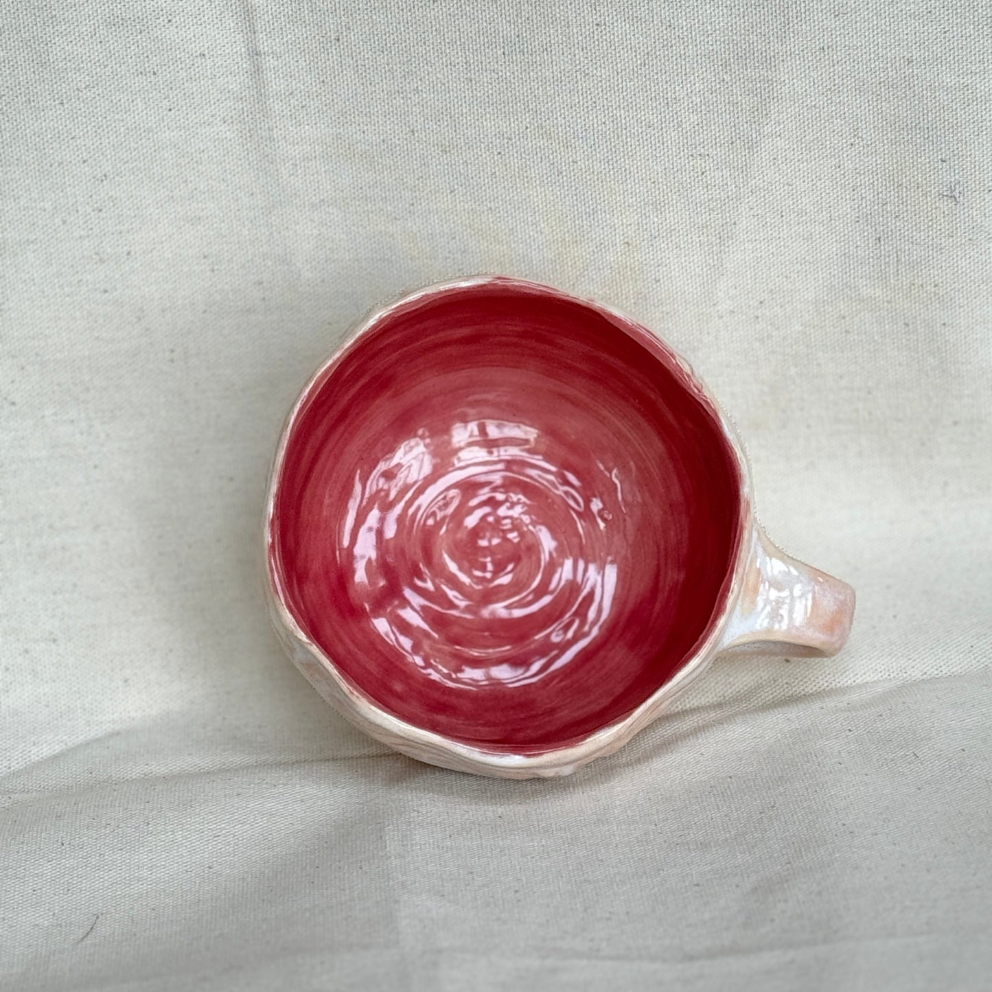 pink ceramic mug with a handle on a light gray fabric background