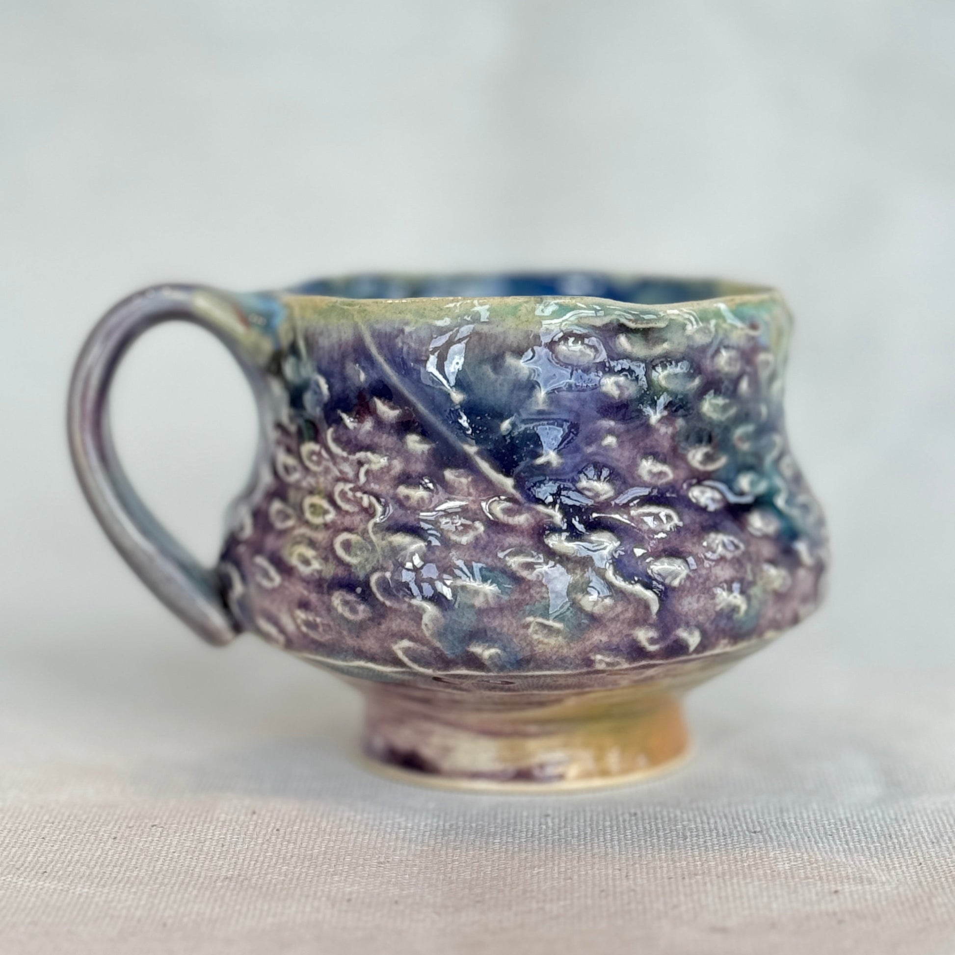 Handmade ceramic mug with textured surface on a light background