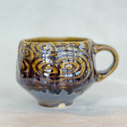Ceramic mug with swirling brown and beige design on a light background