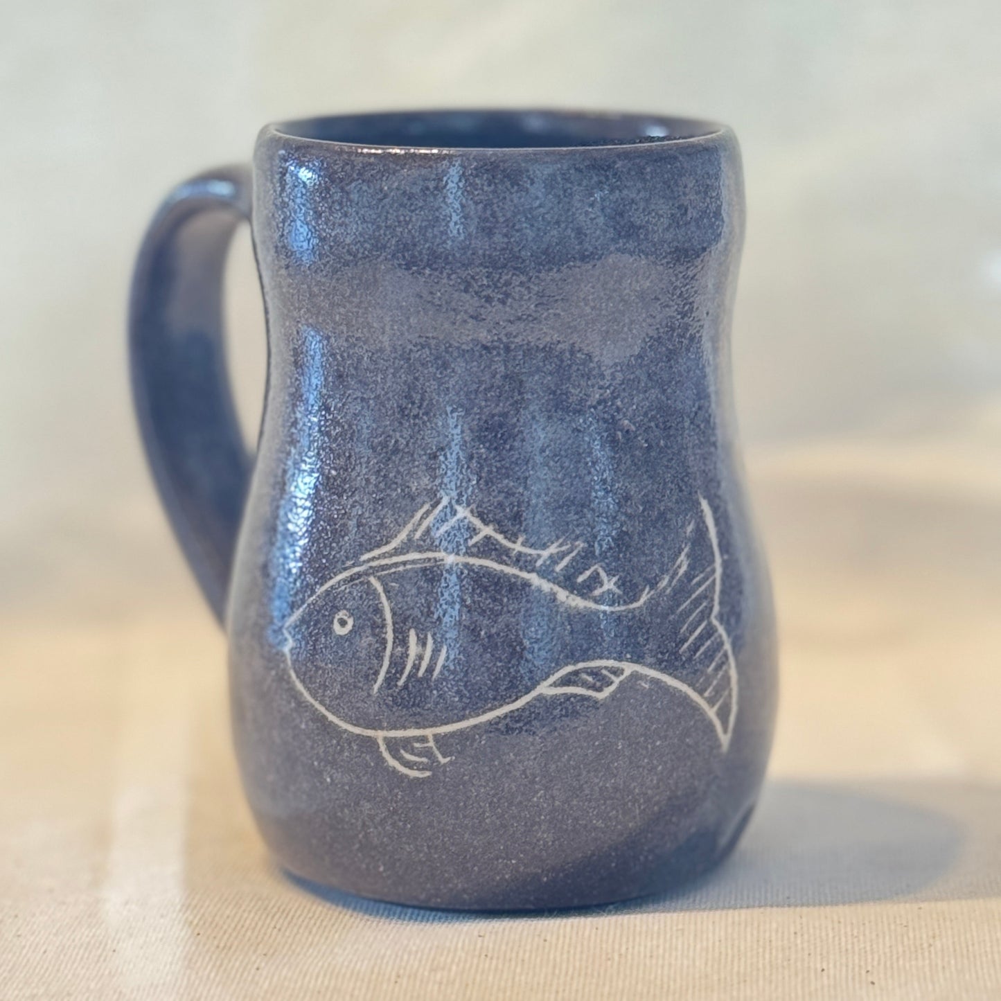 Blue ceramic mug with fish design on a beige surface