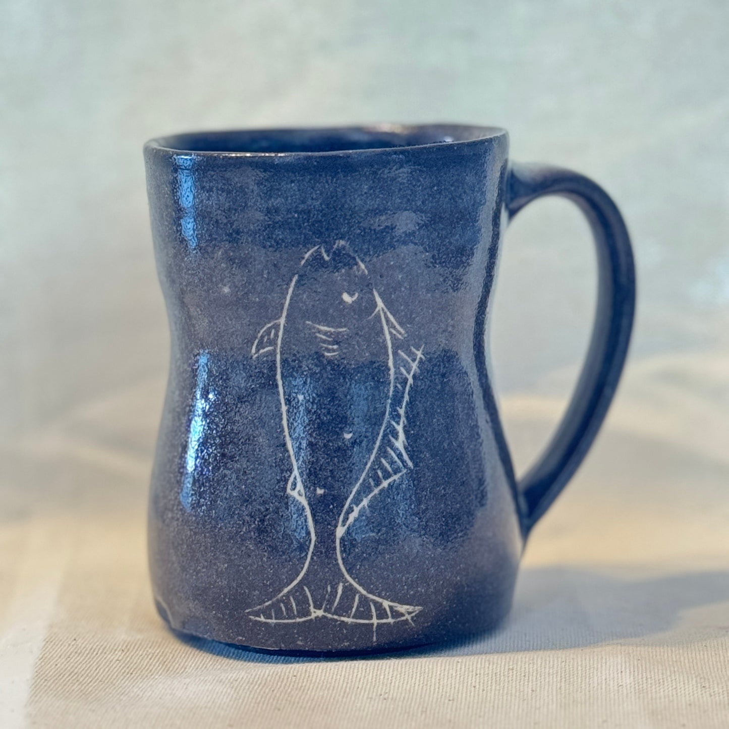 Blue ceramic mug with fish design on a beige surface