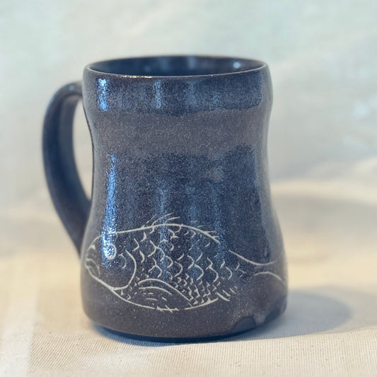 Blue ceramic mug with fish design on a beige surface