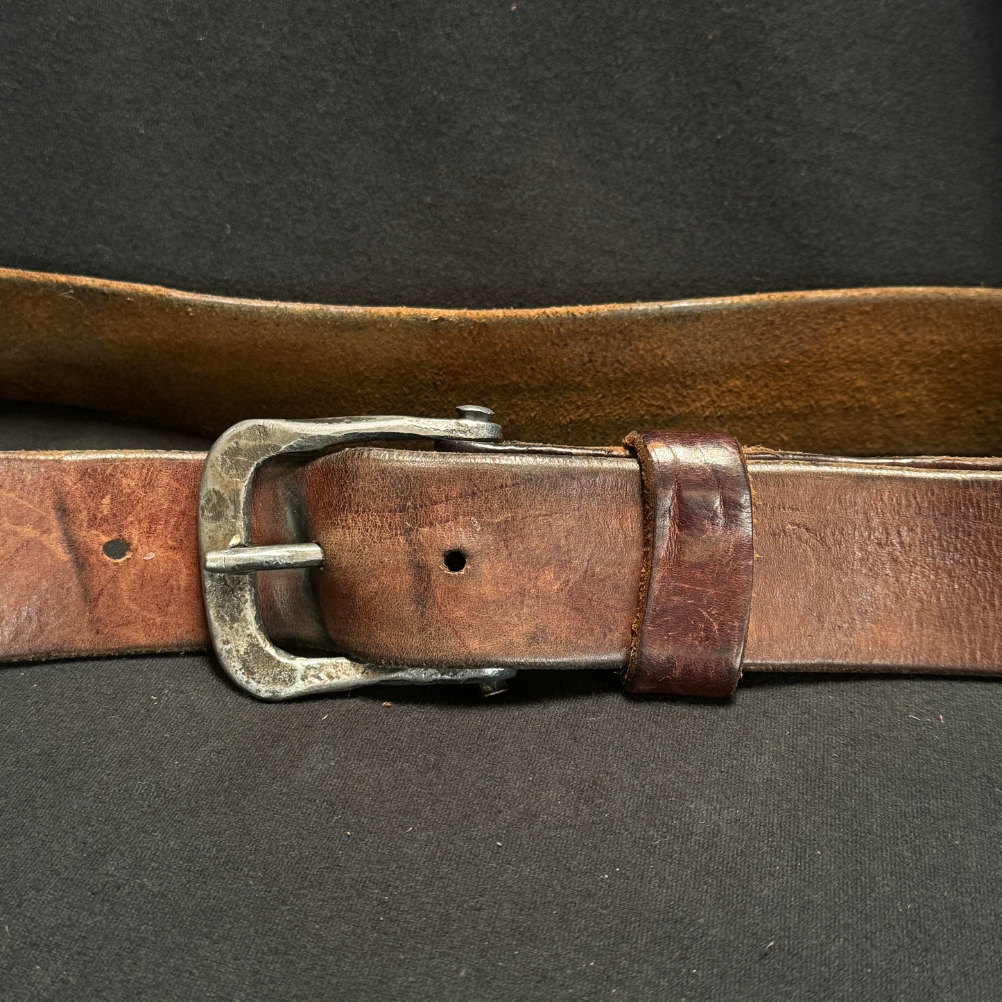 Brown leather belt with a silver buckle on a dark background