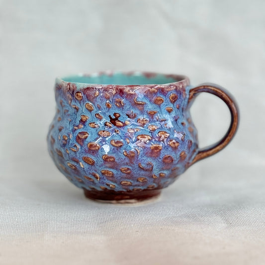 Ceramic mug with blue and brown speckled pattern on a light gray background