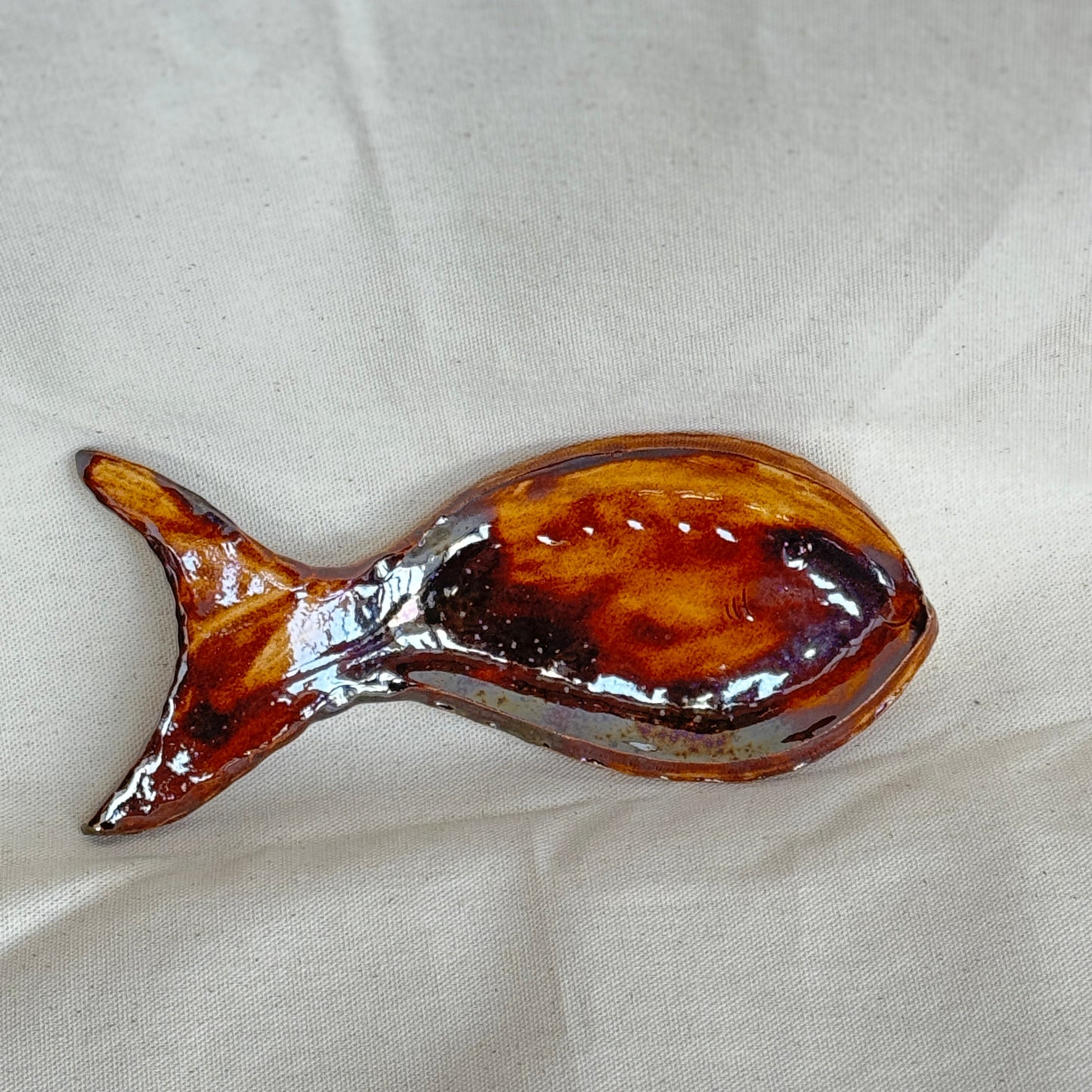 Brown fish-shaped spoon rest on a beige fabric background