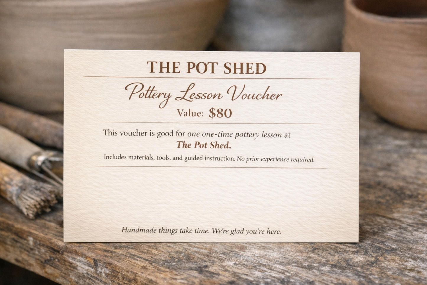 Pottery lesson voucher from The Pot Shed on a wooden surface with pottery items.