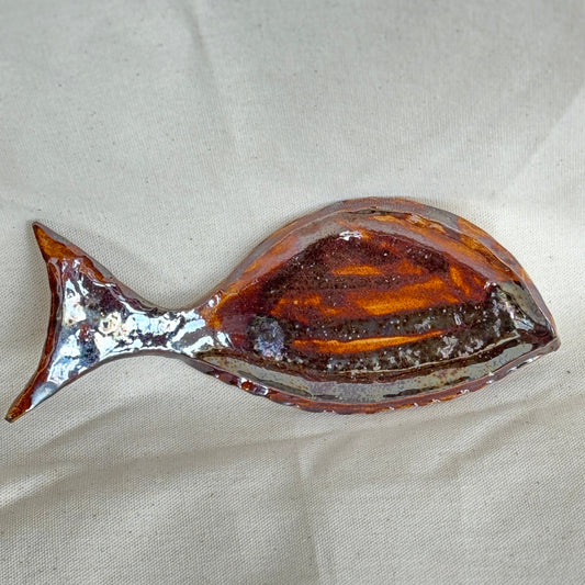 Decorative fish-shaped spoon rest with a metallic finish on a beige fabric background