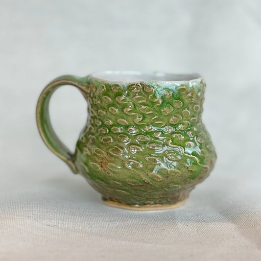 Green ceramic mug with textured surface on a light gray background