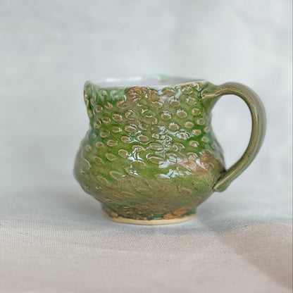 Green ceramic mug with textured surface on a light gray background