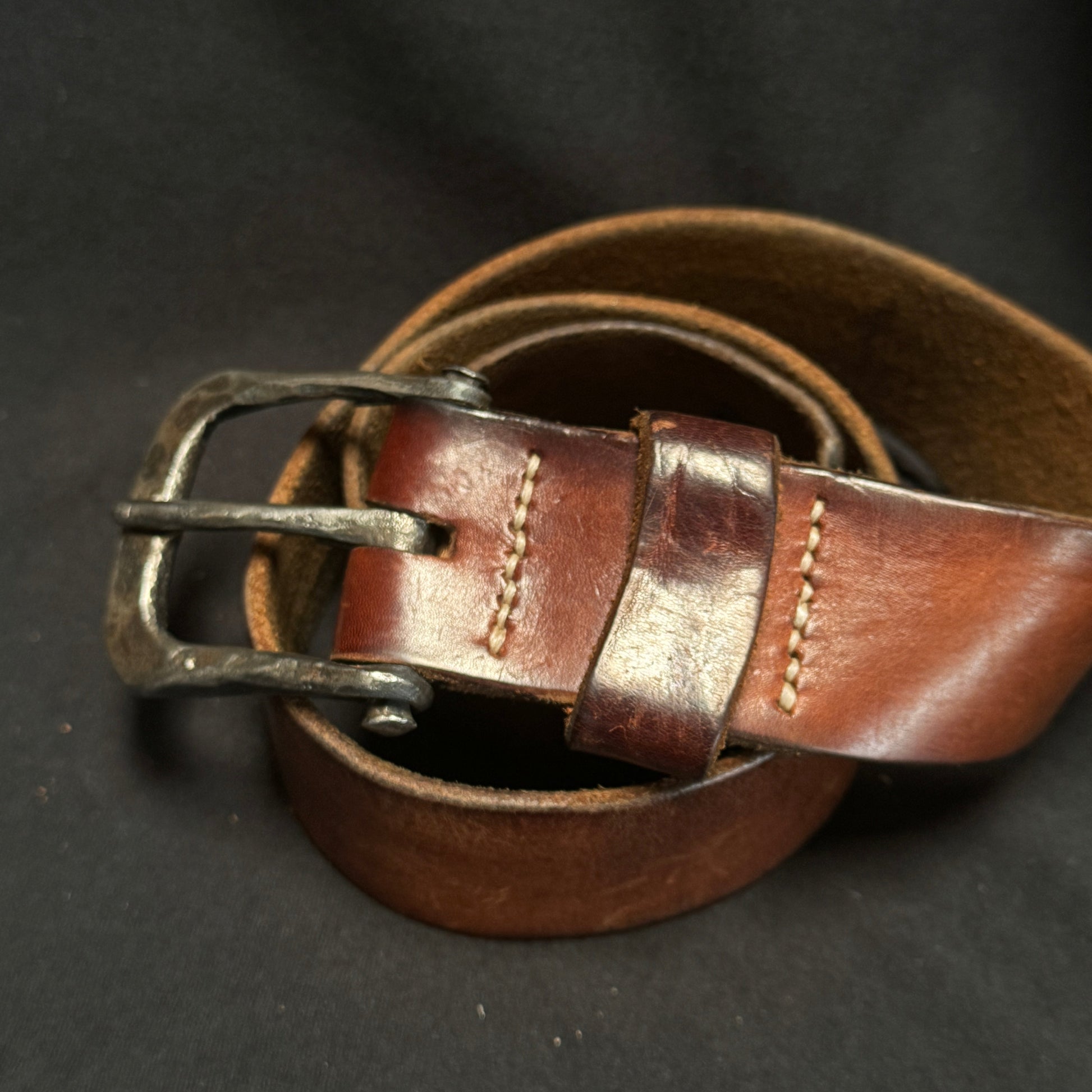 Brown leather belt with a metal buckle on a dark background