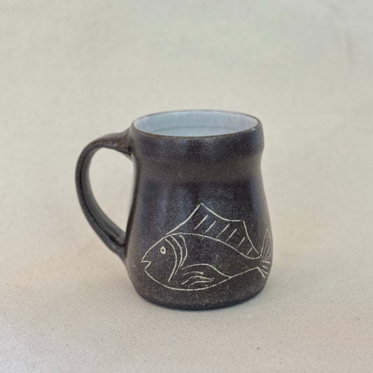 Black ceramic mug with fish design on a white background