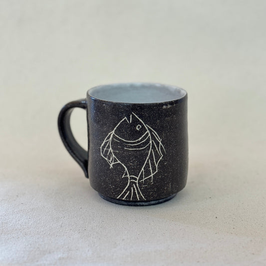 Black mug with a white fish design on a light gray background