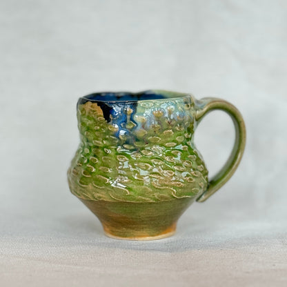Green ceramic mug with textured surface on a white background