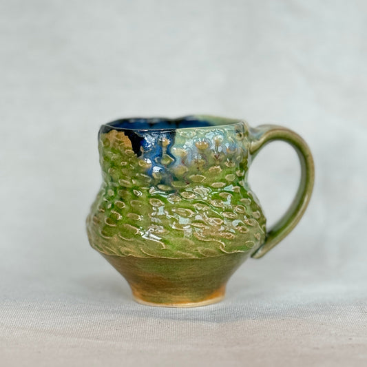 Green ceramic mug with textured surface on a white background