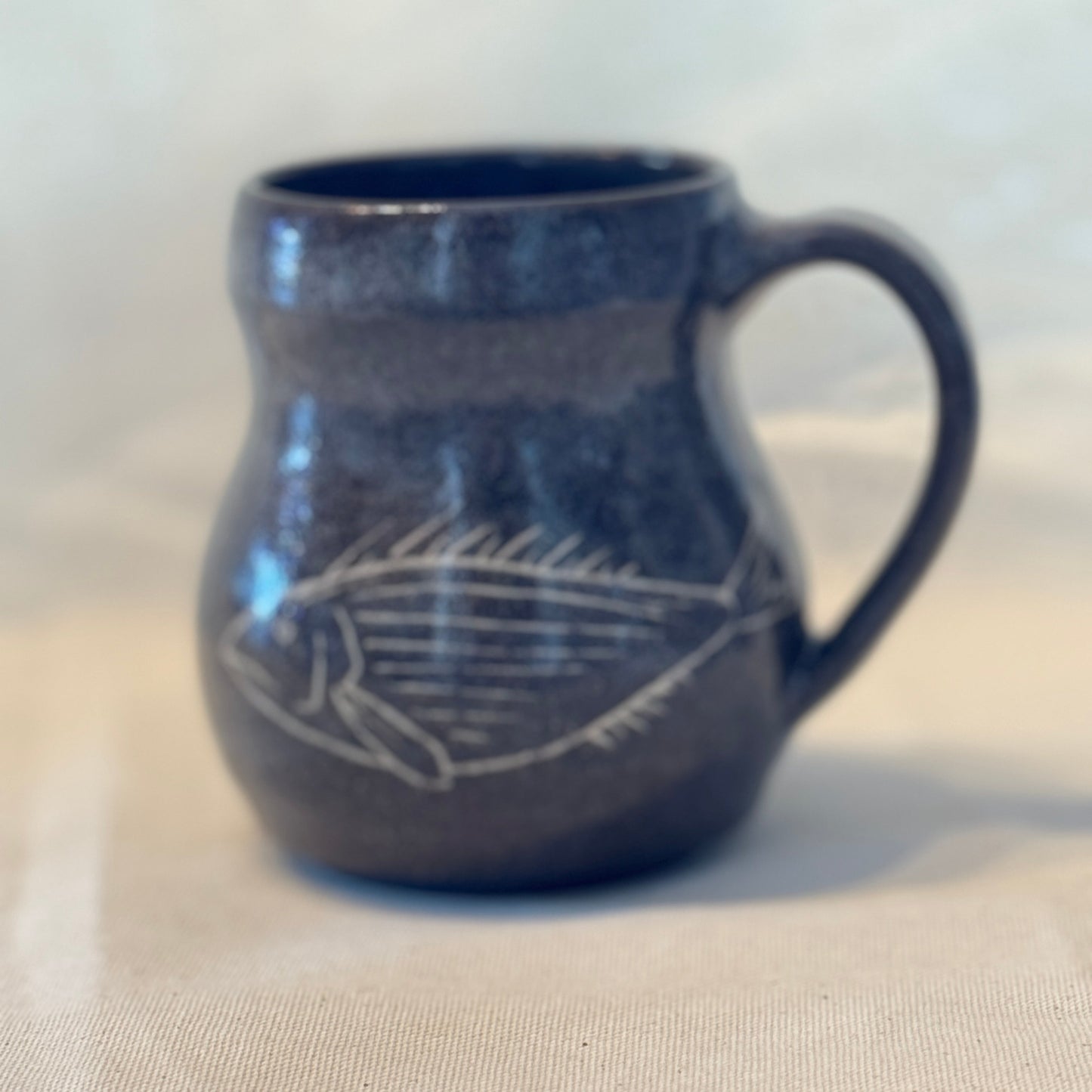 Blue ceramic mug with a white fish design on a beige surface