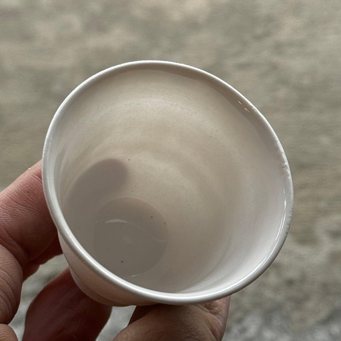 Hand holding a white ceramic cup against a neutral background