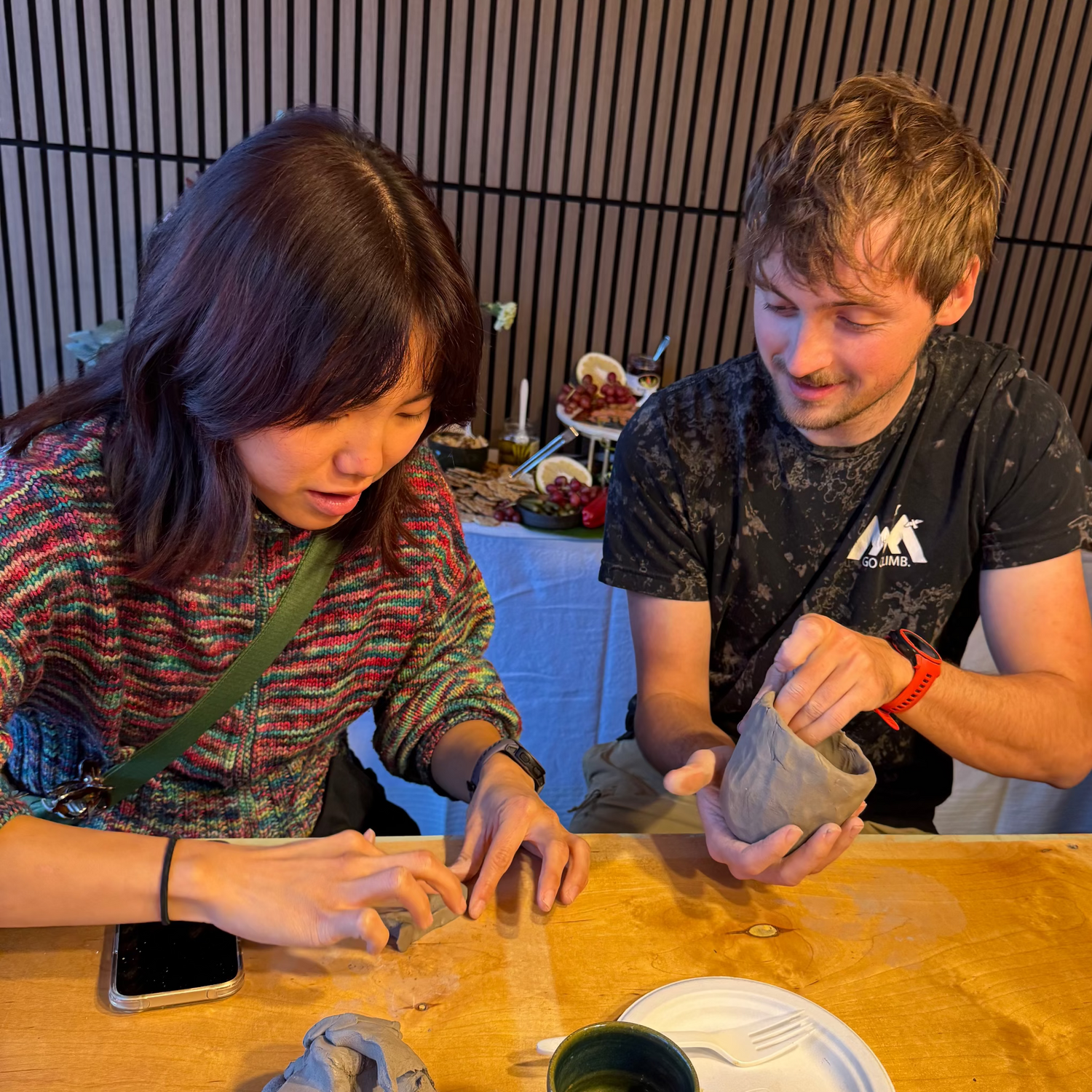 Two people working with clay at a table in a casual setting