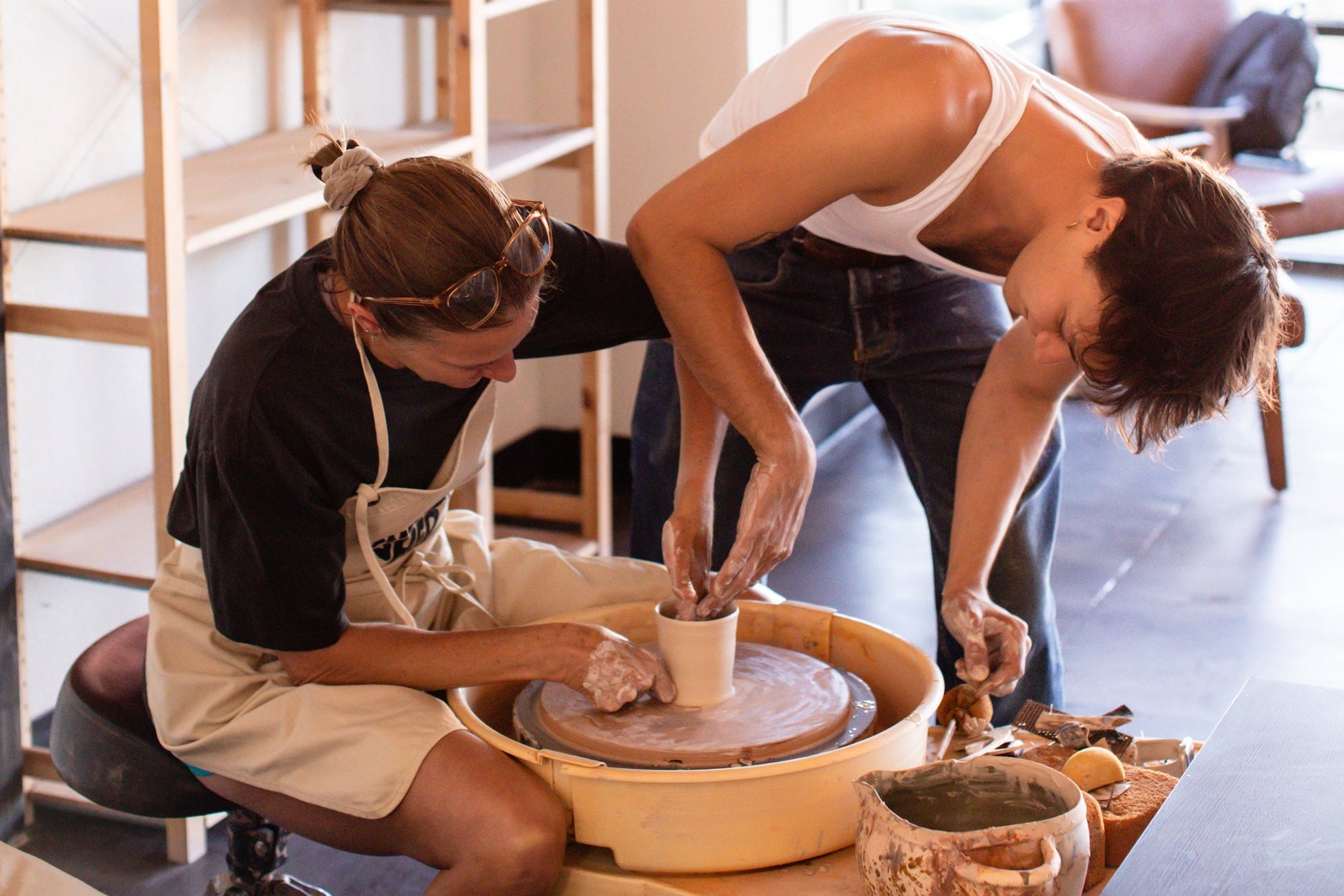 Two people working with clay on a pottery wheel in a studio setting.