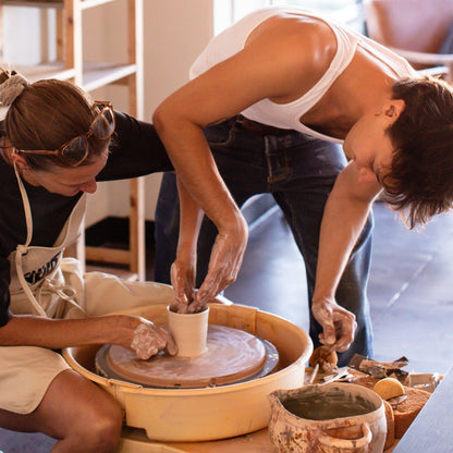 Two people working with clay on a pottery wheel in a studio setting.