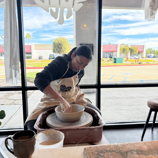 Person working with clay on a pottery wheel in a studio with large windows.