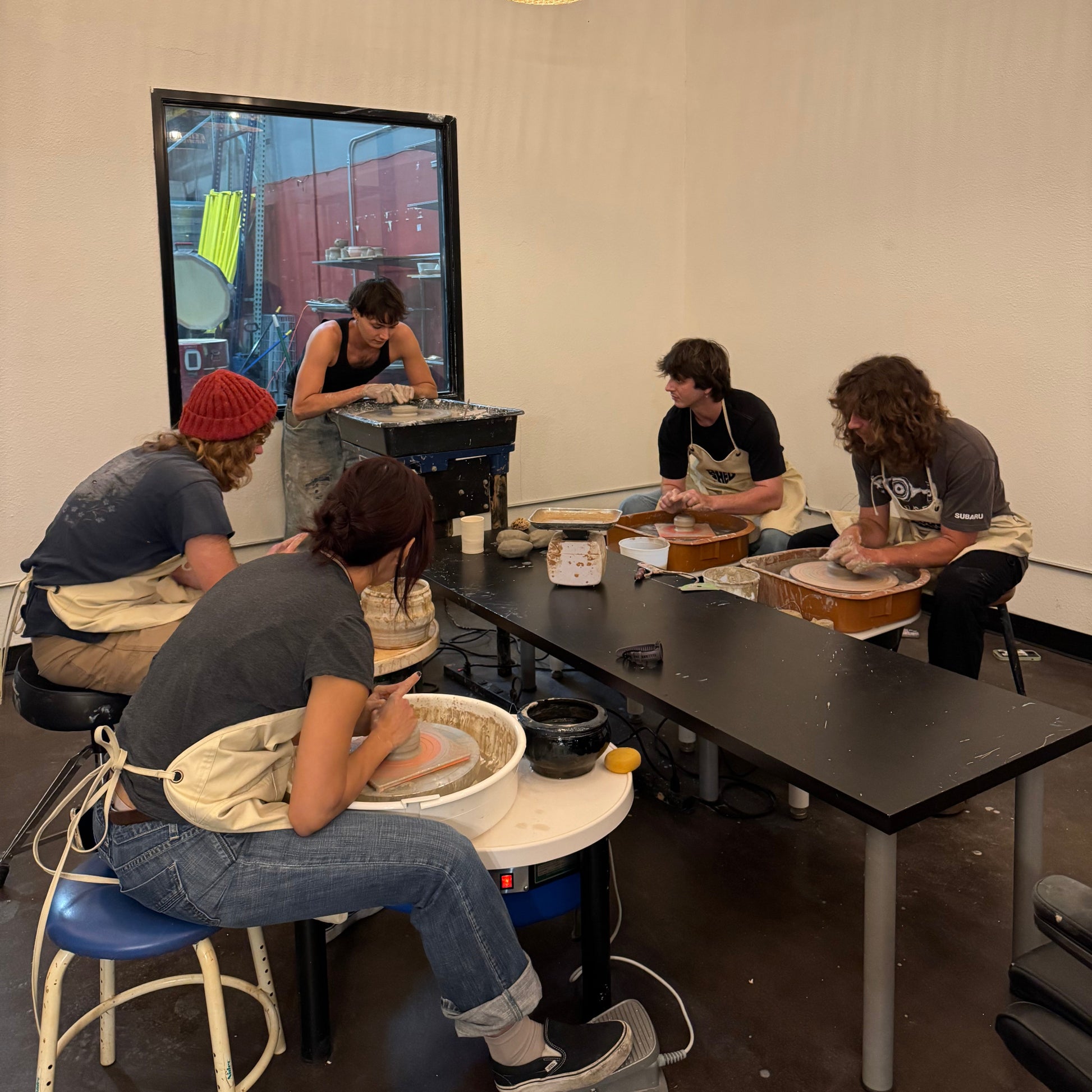 Group of people working on pottery in a studio with wicker lamps.