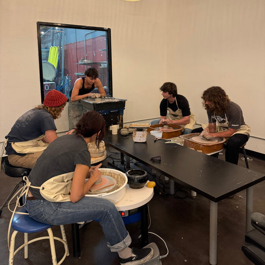 Group of people working on pottery in a studio with wicker lamps.