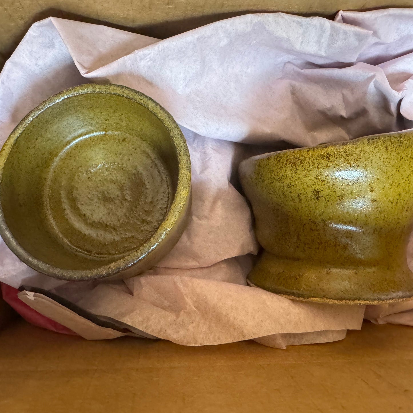Two green ceramic bowls inside a cardboard box with tissue paper.