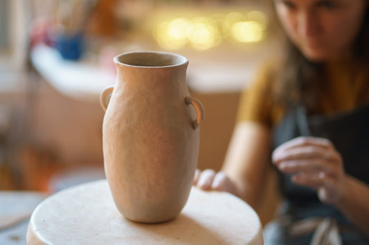 Pottery wheel with a clay vase being shaped, blurred background of a potter at work.