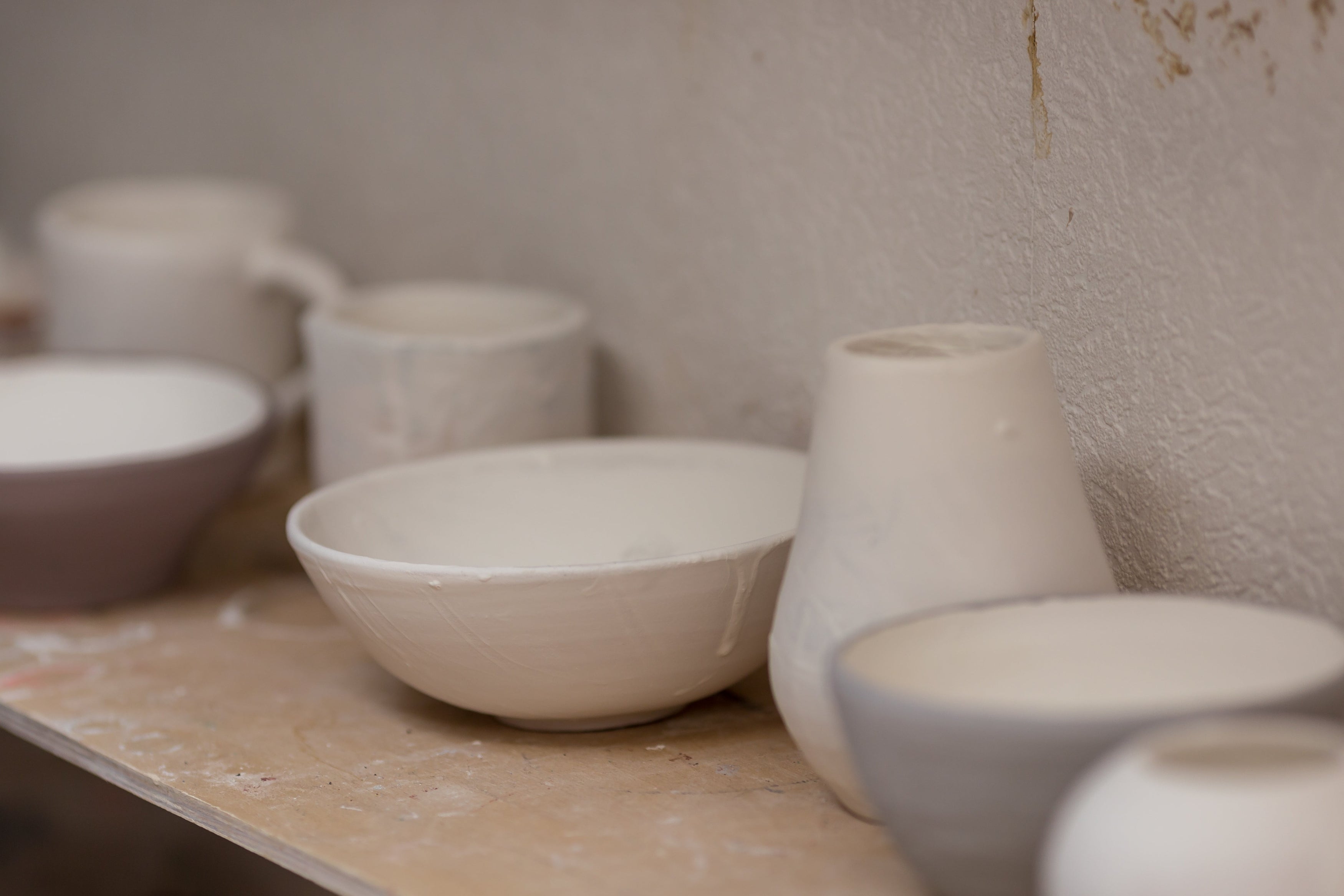 White ceramic bowls and vases on a wooden surface with a textured wall background