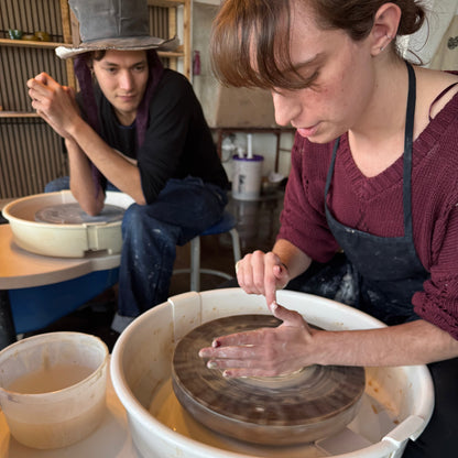 Two people working on pottery in a studio setting.