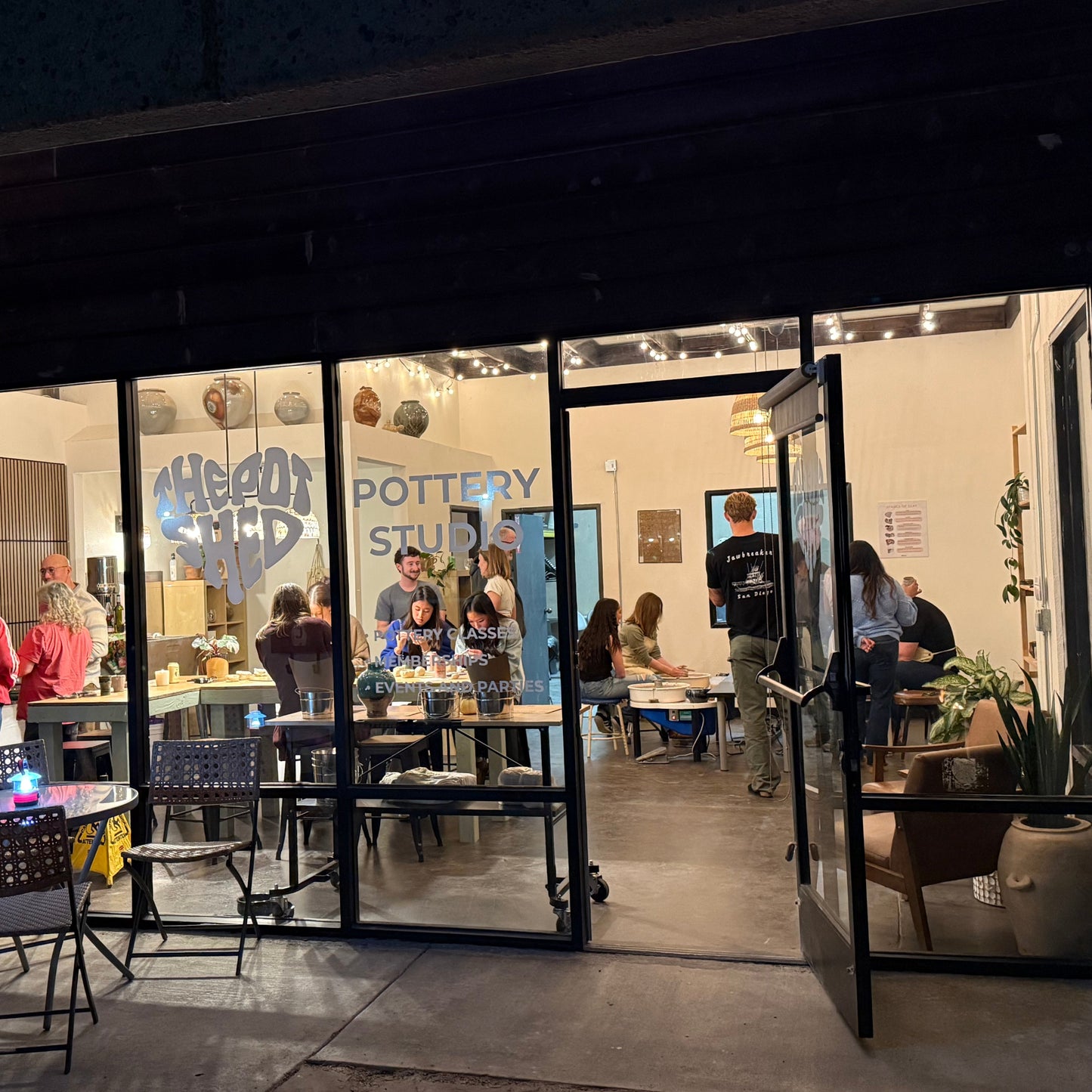 People inside a pottery studio viewed from outside through large glass doors.